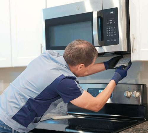 Technician performing microwave repair service for a residential kitchen appliance