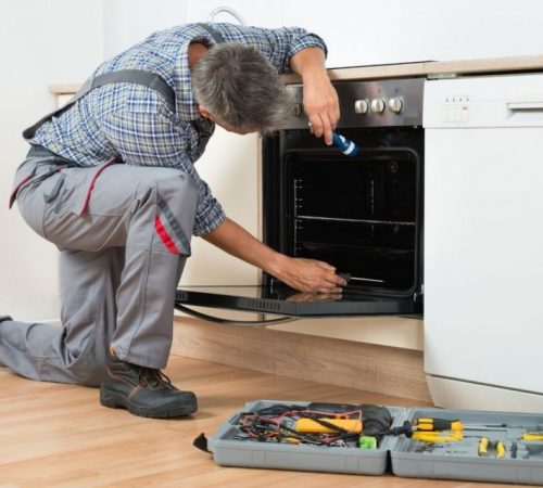 Technician performing professional oven repair service with tools in a residential kitchen
